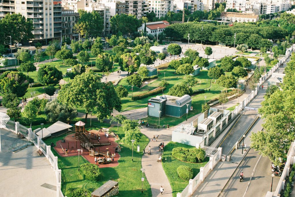 Aerial view of an urban park. Green grass and trees, apartment blocks in the background, roads in the foreground