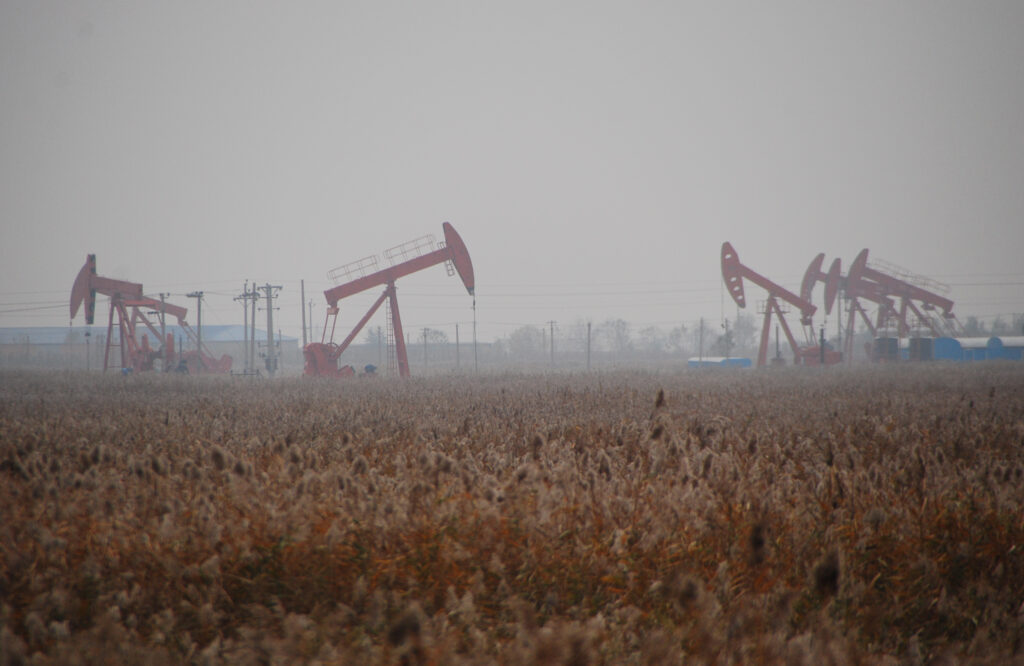 Red oil derricks in use in a field with corn in the foreground.